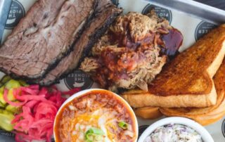 A tray of smoked brisket, pulled pork, and Texas toast, highlighting The Pioneer BBQ's passion for authentic barbecue.